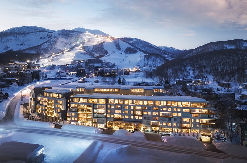 ニセコのスキーリゾートと雪山に囲まれたホテルの風景（出典：ski.com）